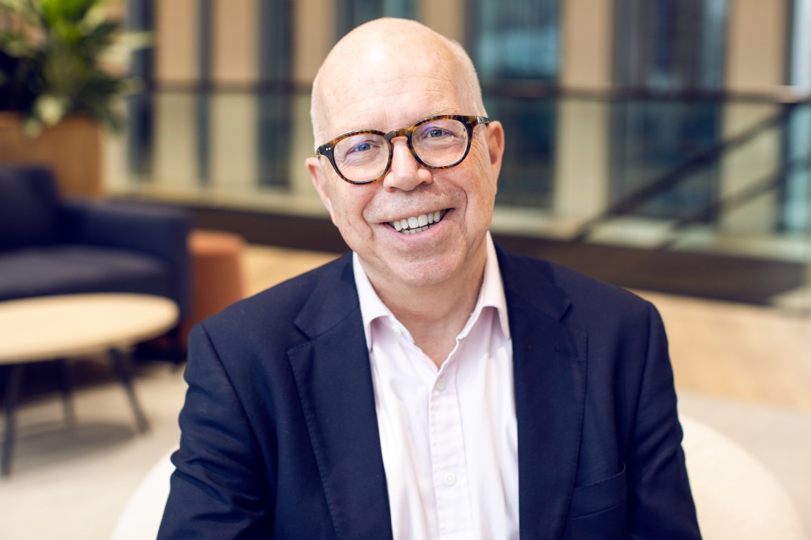 Smiling man wearing glasses and a dark blazer in a modern office setting
