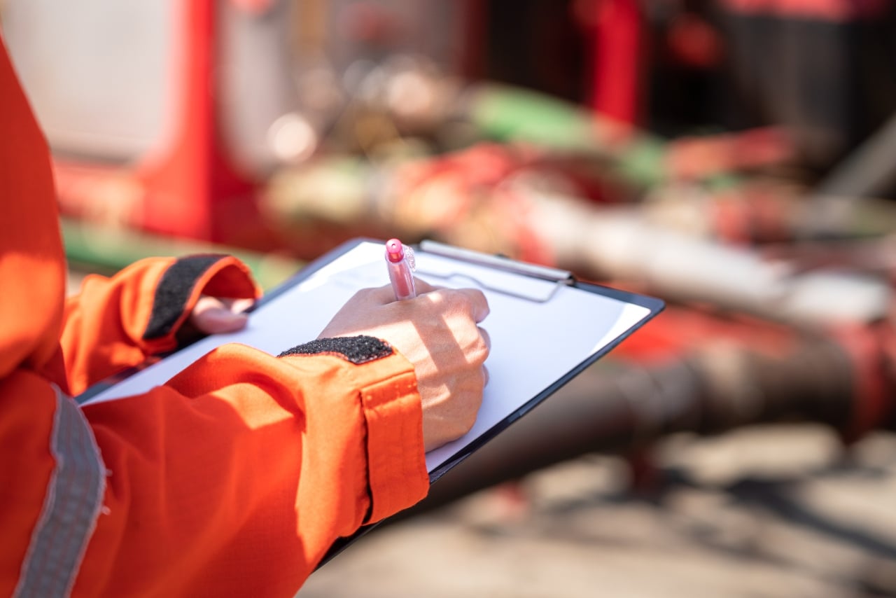 Person in orange safety jacket writing on a clipboard during an audit