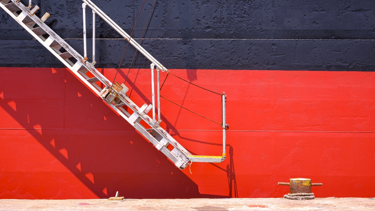 White gangway ladder attached to a ship with red and black hull