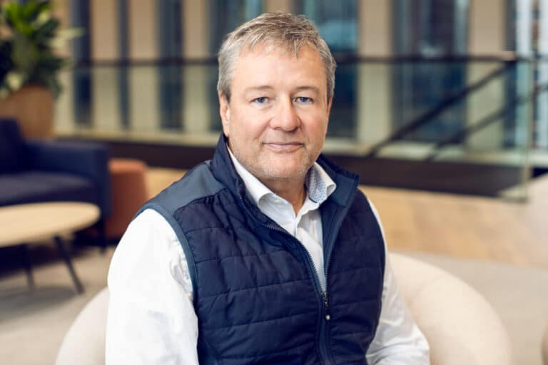 Man wearing a navy vest and white shirt sitting indoors